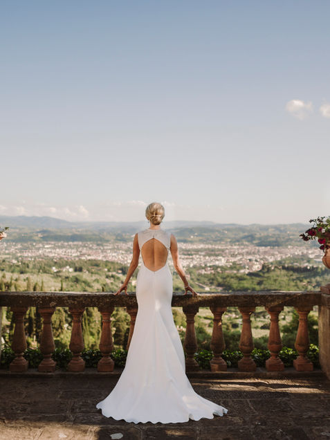 The bride in a white dress looks at the horizon from a panoramic terrace above Florence, bathed in golden light.