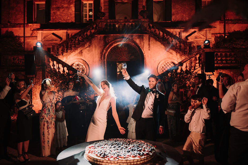 Bride and groom cutting wedding cake under dramatic lighting at Villa Cetinale, Tuscany