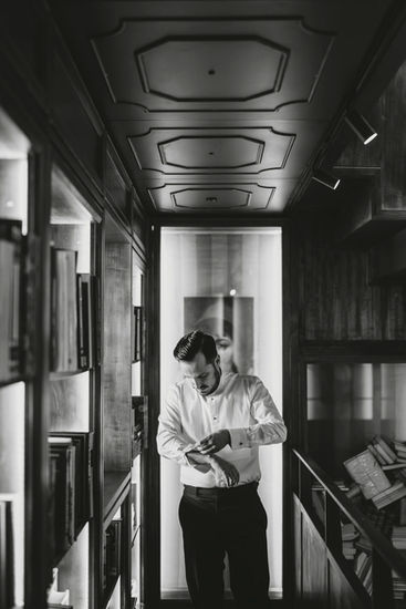 Man in white shirt looking at his watch, corridor with books, riccardopieri.