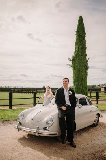 Bride and groom by their vintage car in the golden sunset light.