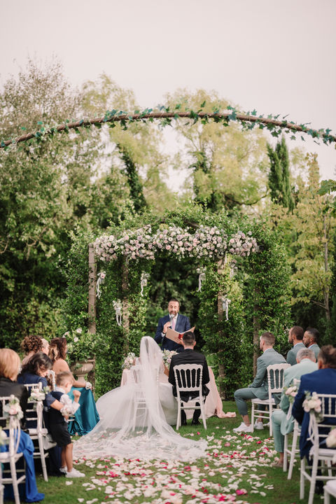 Outdoor wedding ceremony in Tuscany with floral arch and elegant garden setting