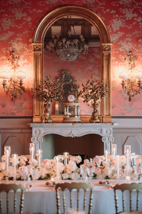 Elegant dining table with white floral centerpieces, candles, gilded mirror.