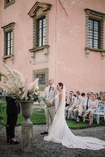 Bride and groom standing at the ceremony; bride has a long train.