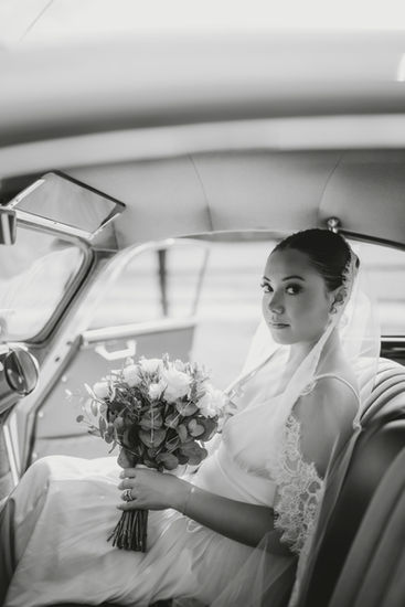 Black and white bride sitting in a vintage car holding her bouquet.