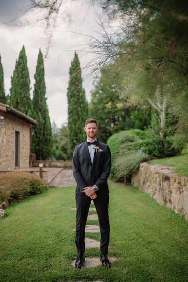 Groom in black suit poses, Casa Cornacchi Tuscan wedding, greenery background. riccardopieri