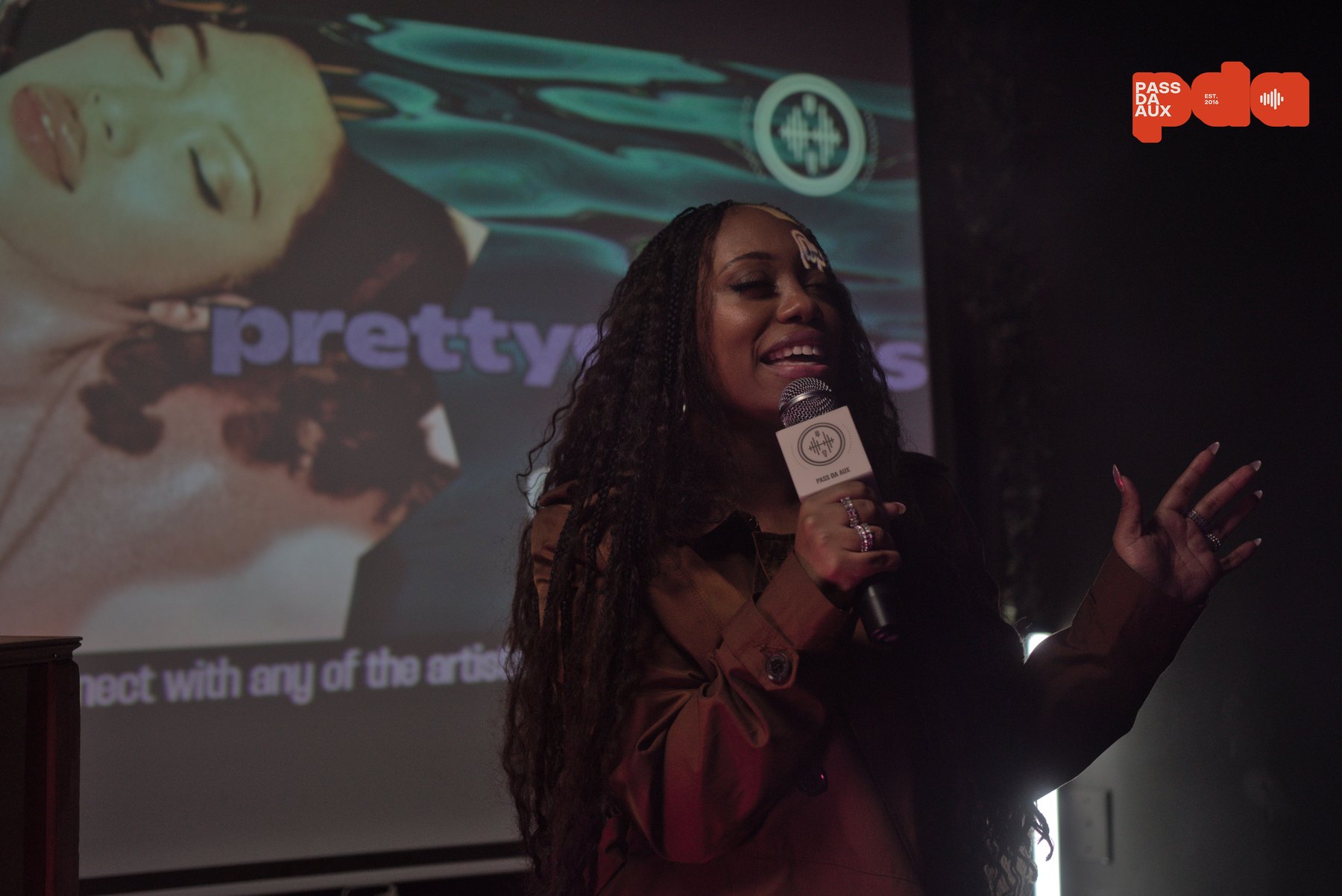 prettygenius speaking onstage at the Pass Da AUX Artist Showcase