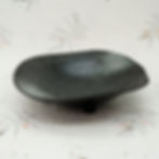 Three-feet ceramic fruit bowl by EngiCrafts with a matte black finish, irregular shape, and tripod base for artistic flair.