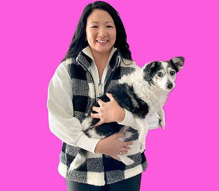 Korean-American female dressed in black and white holding a small black and white dog against a pink background