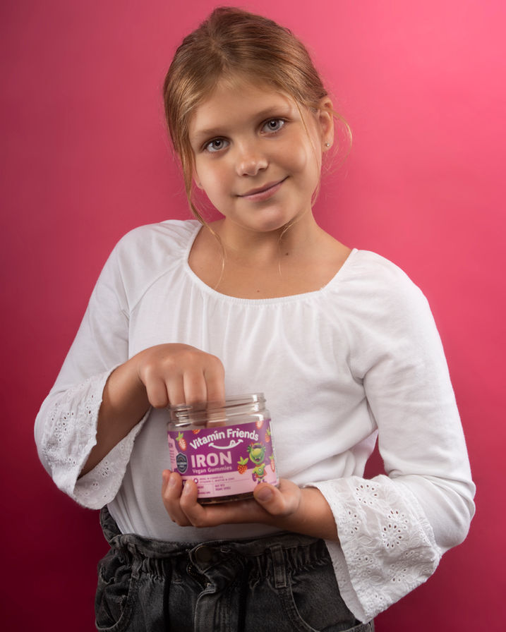 Smiling girl holding a jar of vitamins against a pink background