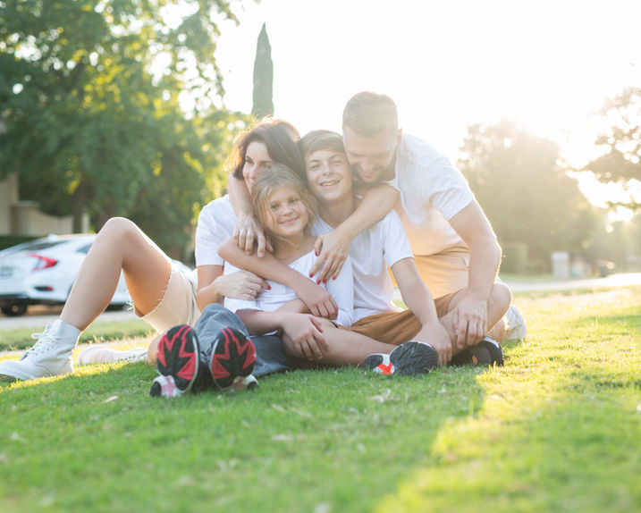 Family sitting on grass during picnic under sunlight.