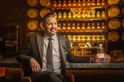  Man sitting in whiskey bar with shelves of bottles.