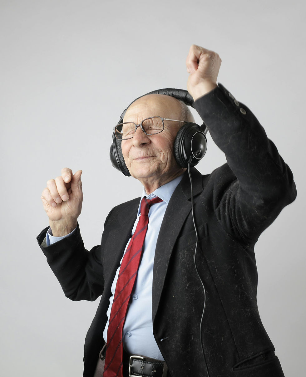 Old man in a suit with headphones on with his eyes closed and his arms held up. He appears to be dancing to the music he is listening to.