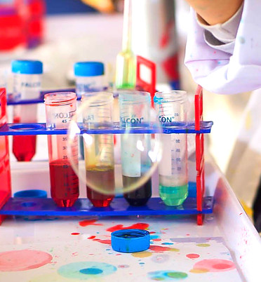 A child's hand creating a bubble. Next to some colourful test tubes from the SciencePlay Kids kits.