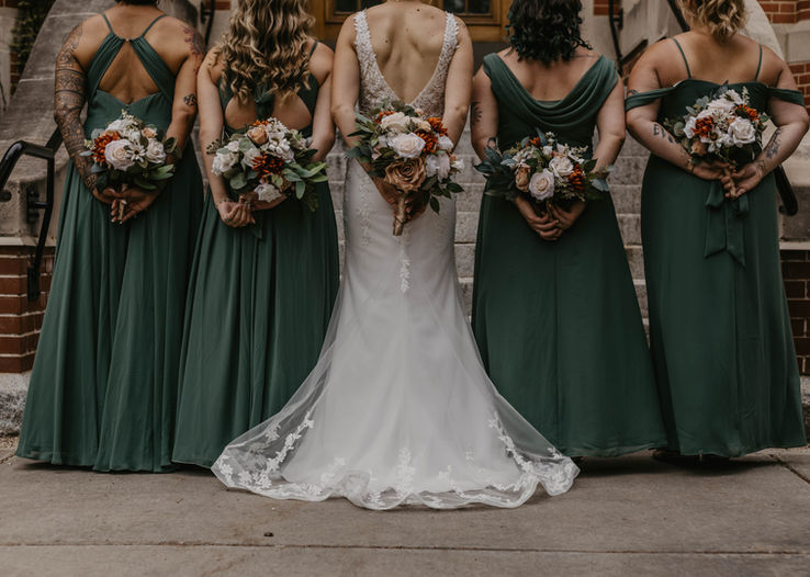 The bride and her bridesmaids hold stunning bouquets featuring white flowers paired with rich fall colors, such as deep reds, oranges, and yellows. The bride’s bouquet is a beautiful blend of white blooms and autumn-hued accents, while the bridesmaids’ bouquets complement with similar tones, adding warmth and vibrancy to the scene. The fall-inspired florals enhance the elegance and seasonal charm of the moment.