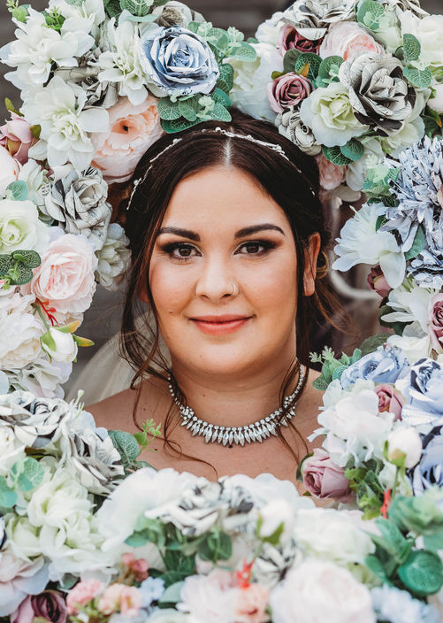 Bride stands surrounded by bouquets framing her face in Saskatoon Saskatchewan