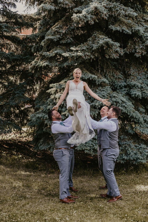 groomsmen playflully toss the bride into the air and stand waiting too catch her 