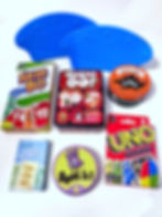 Various card games arranged on a white surface, including Skip-Bo, Sushi Go!, Uno, Go Fish, Spot it!, and Dealing Dinos. Two blue cardholders.