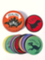 Round card game tins "Dealing Dinos" and "T. Rex" with illustrated dinosaurs on colorful cards, laid out on a white surface.