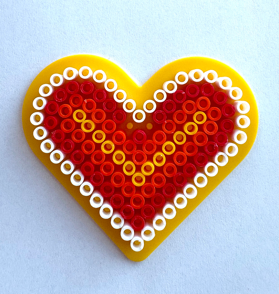 Yellow heart made from beads on a light blue background. Beads vary in colors: red, orange, and white, forming a pattern within the heart.