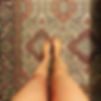 Photograph of a Persian rug and the artist's own legs, in viewers perspective with the feet landing in the rug's central medallion.