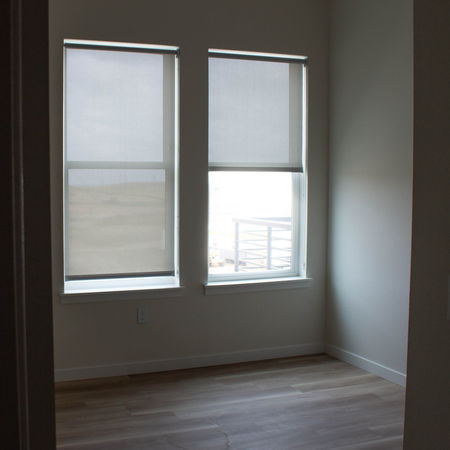 An empty apartment unit featuring light LVP floors and beige walls, the picture is to emphasize the beige manually operated roller shades.