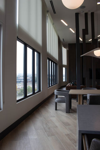 Apartment building amenities area featuring minimalist gray seating and lighting and while manually operated roller shades.