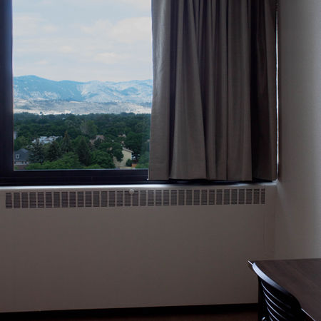 college dormitory empty aside from newly installed blackout drapery that is pleated and a metallic light grey color