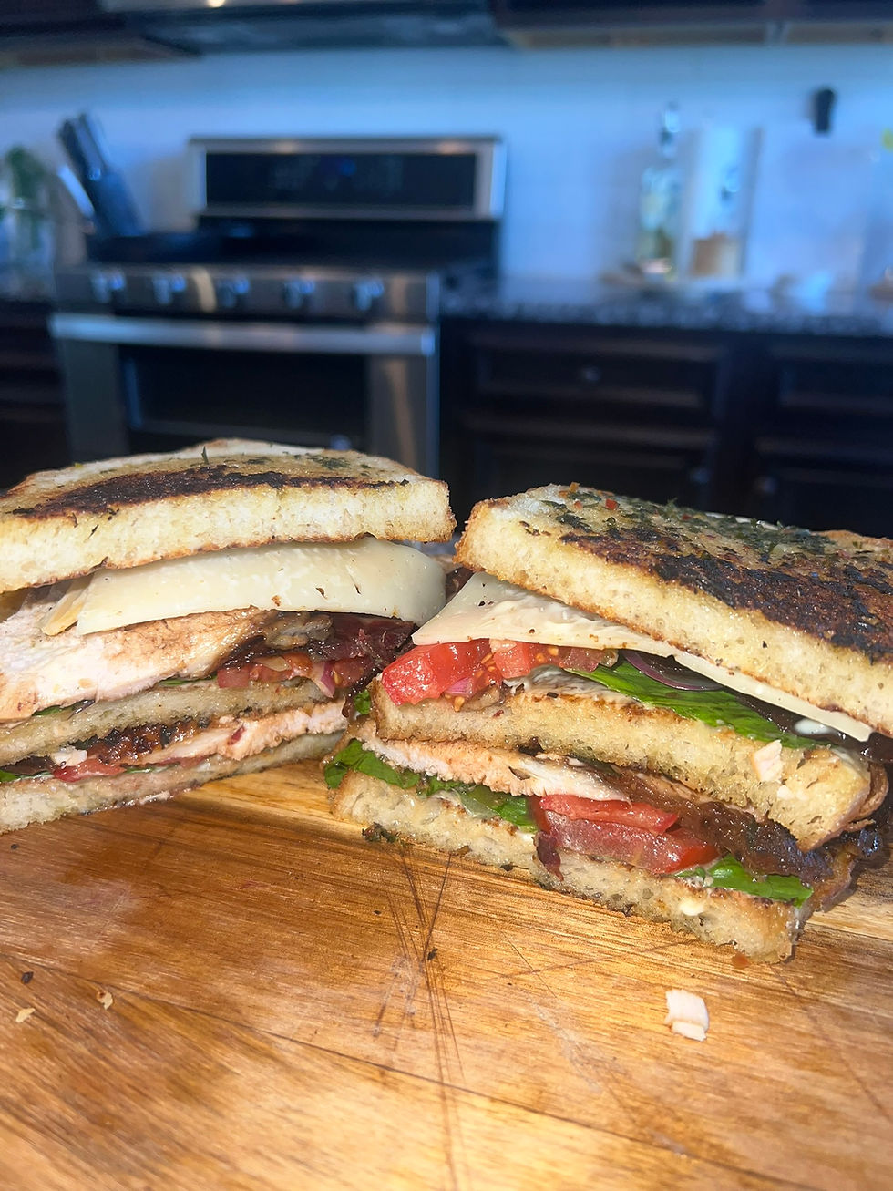 Stacked jerk-seasoned turkey club sandwich made with herb butter toasted sourdough, beef bacon, havarti and colby cheese, lettuce, and tomatoes