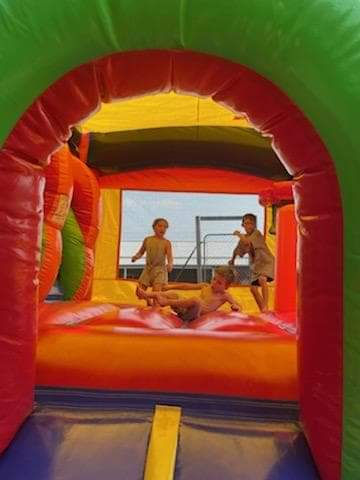 Thumbnail: Kids bouncing in multi-colored inflatable bounce house on green grass in Michigan 48880