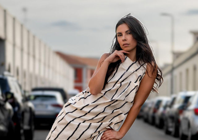 Shooting fotografico del brand Marjena, con modella che indossa un abito bianco a righe nere e drappeggio sul davanti