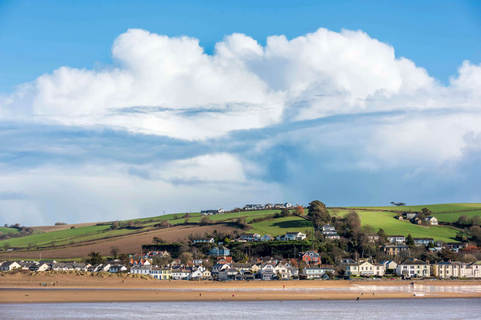 Coastal village with homes and a sandy beach under a cloudy sky.