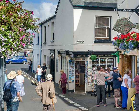 A small queue of people outside aTraditional fish and chip shop with a fish-shaped swinging street jewelry