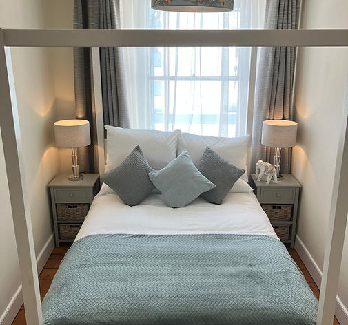 White four-poster bed with blue blanket, lamps, and patterned light