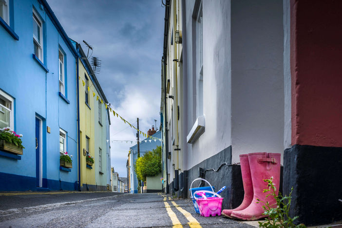 Colorful buildings on a narrow street with pink rain boots and toys.