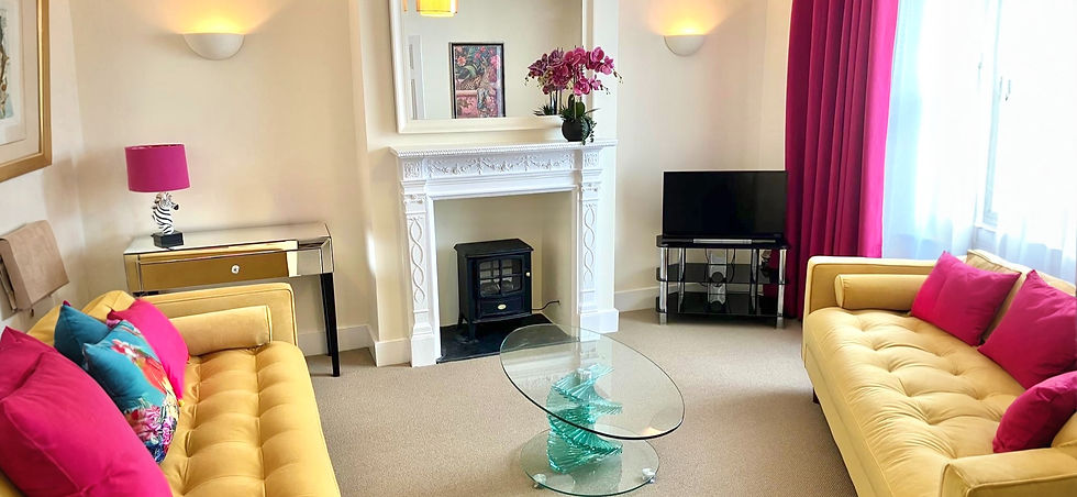 Living room with yellow sofas, pink pillows, fireplace, and TV