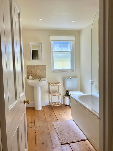 Cream bathroom with wooden floor, white sink, toilet, and tub