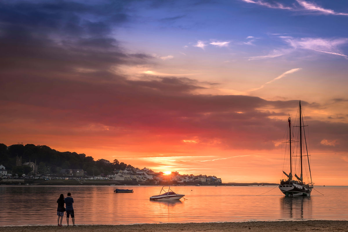 Couple watching sunset near boats on the water with colorful sky