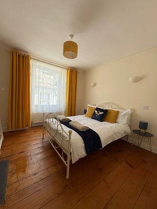 Bright bedroom with white metal bed, yellow accents, and wooden floor.
