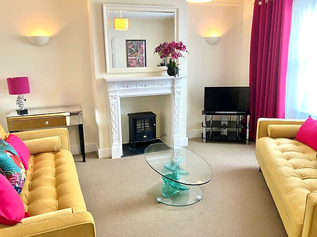 Living room with yellow sofas, pink accents, and fireplace