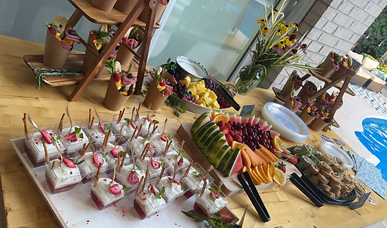 A grazing table with fresh fruits, charcuterie boxes, and dessert cups