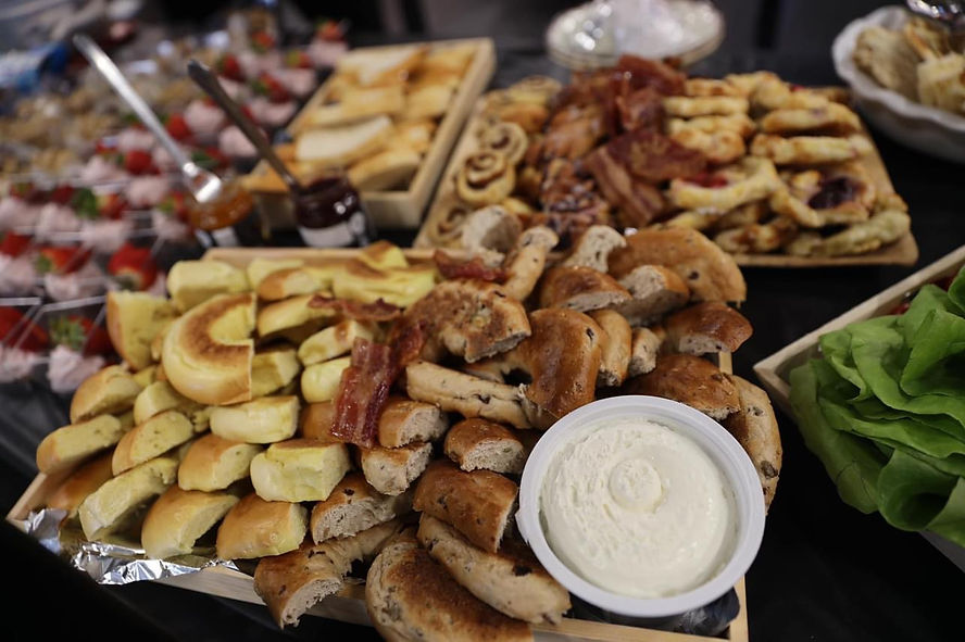 A brunch grazing table with cut up bagels, cream cheese, skewered strawberries, and pastries
