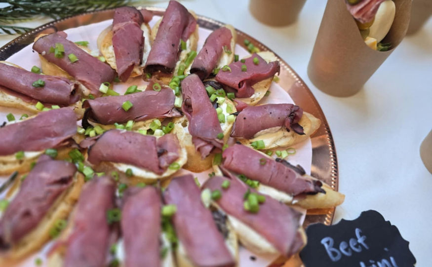 Beef crostini and other appetizers displayed at a catered event with greenery.