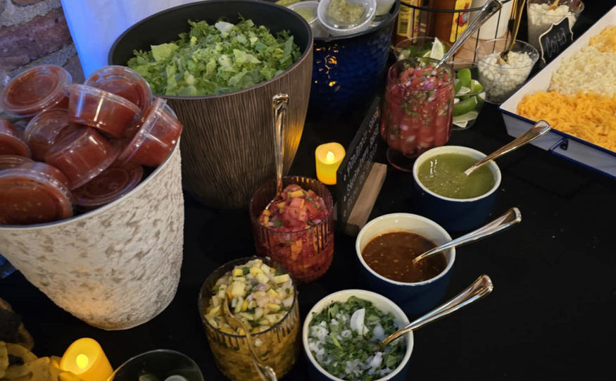Taco fixings including salsa and tomatoes on a black table with lights.