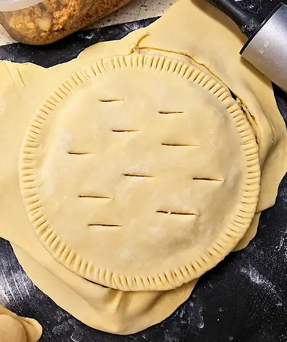Tourtière maison non cuite, préparée avec une pâte brisée végane, sur un plan de travail fariné avec un rouleau à pâtisserie.