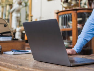 Homem de camisa azul usando um notebook sobre uma mesa de madeira