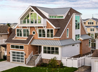 Front-right view of Cascade Shake House in Brigantine, NJ, showing layered rooflines, cedar shingle siding, metal roof accents, and large windows facing the waterfront.