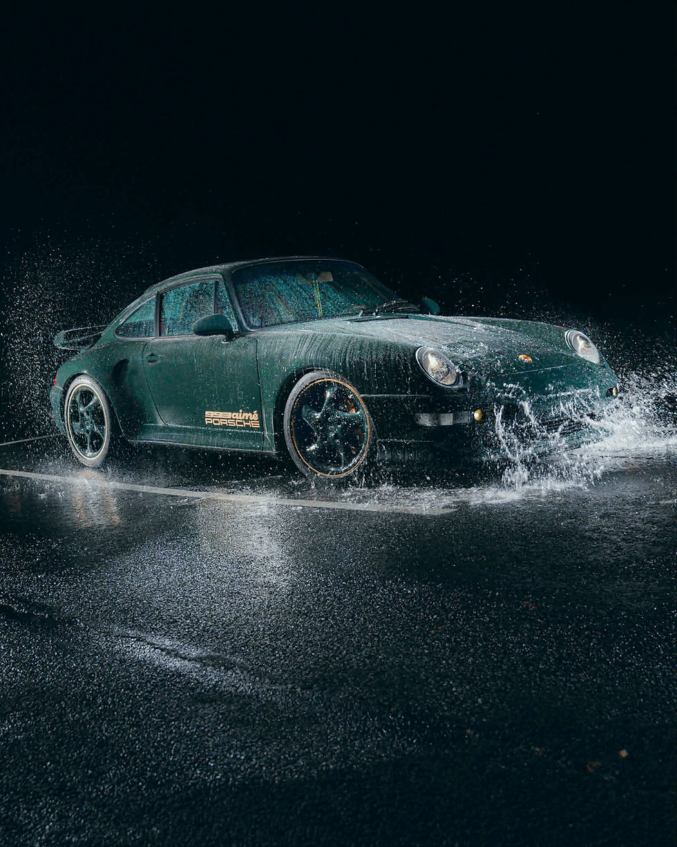 Dark green Porsche 993 with Aimé Leon Dore detailing surrounded by a water splash