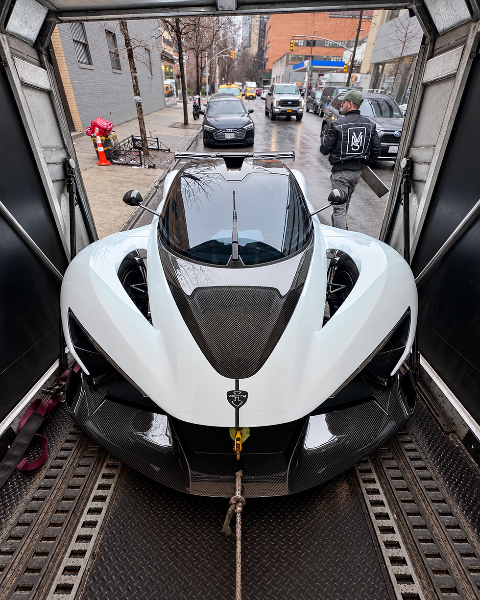 White and carbon-fiber Zenvo hypercar inside a VMS Lux enclosed transporter, with a crew member at the loading area