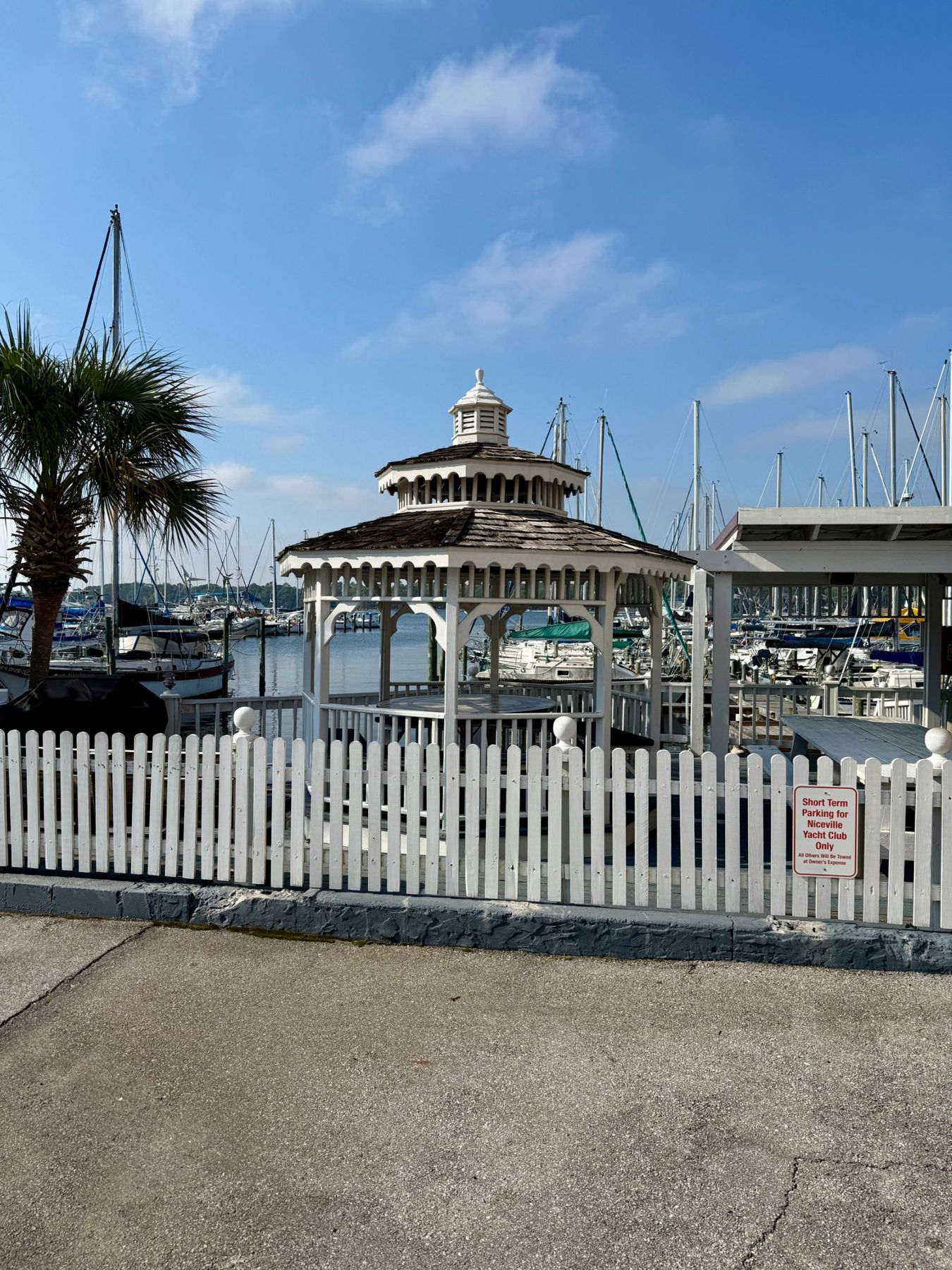 White gazebo behind a picket fence with sailboat masts beyond