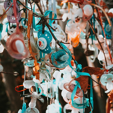 Baum geschmückt mit vielen bunten Schnullern und Bändern im Freien.